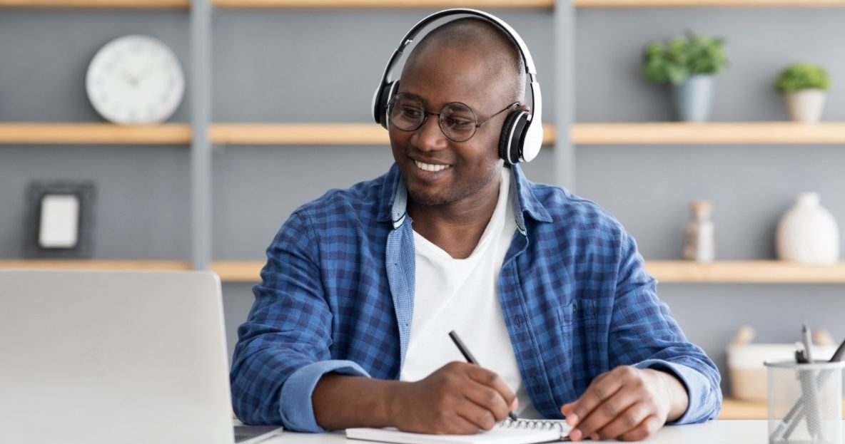 man with headphones taking notes during online course