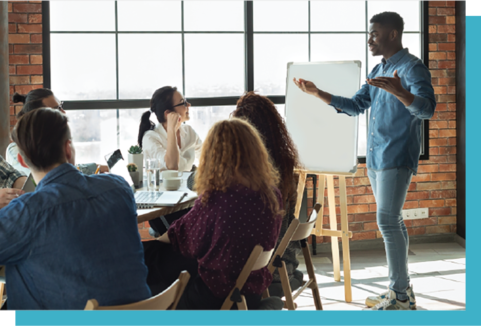 Agile-Leadership-header k A man presents beside a whiteboard to an attentive group seated in a modern, brick-walled room with large windows.