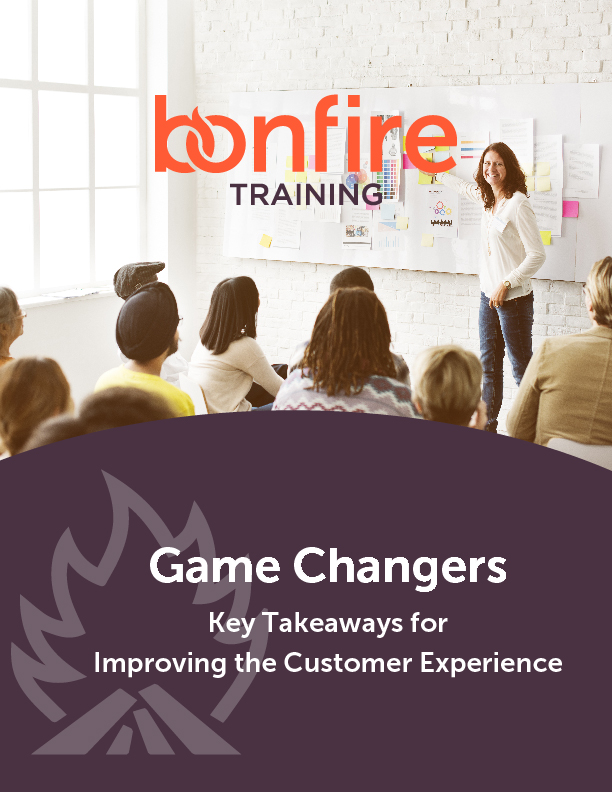 BonfireTraining-Game Changers-WhitePaper-Cover A presenter stands by a board covered with papers, speaking to a seated audience in a bright room. Text: "Bonfire Training. Game Changers: Key Takeaways for Improving the Customer Experience."