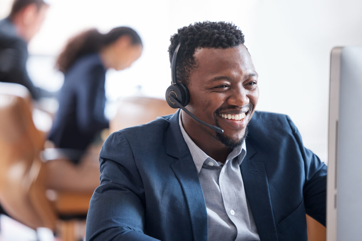 Smiling customer service representative wearing a headset while working at a computer in a call center.