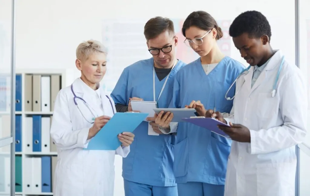Healthcare team reviewing notes and patient documents together in a clinic hallway.