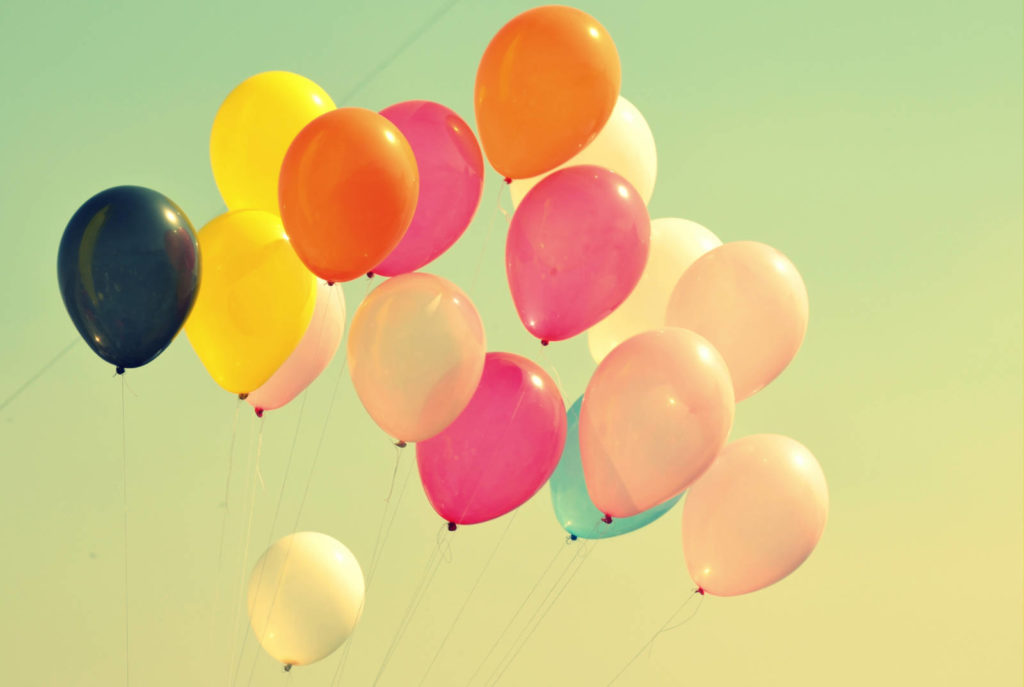 Colorful balloons cluster, floating gently against a clear sky, creating a vibrant, cheerful atmosphere.
