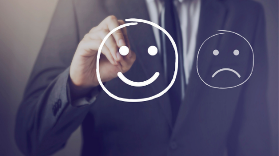 A person in a suit draws a smiling face with a marker, next to a sad face, on a transparent surface.