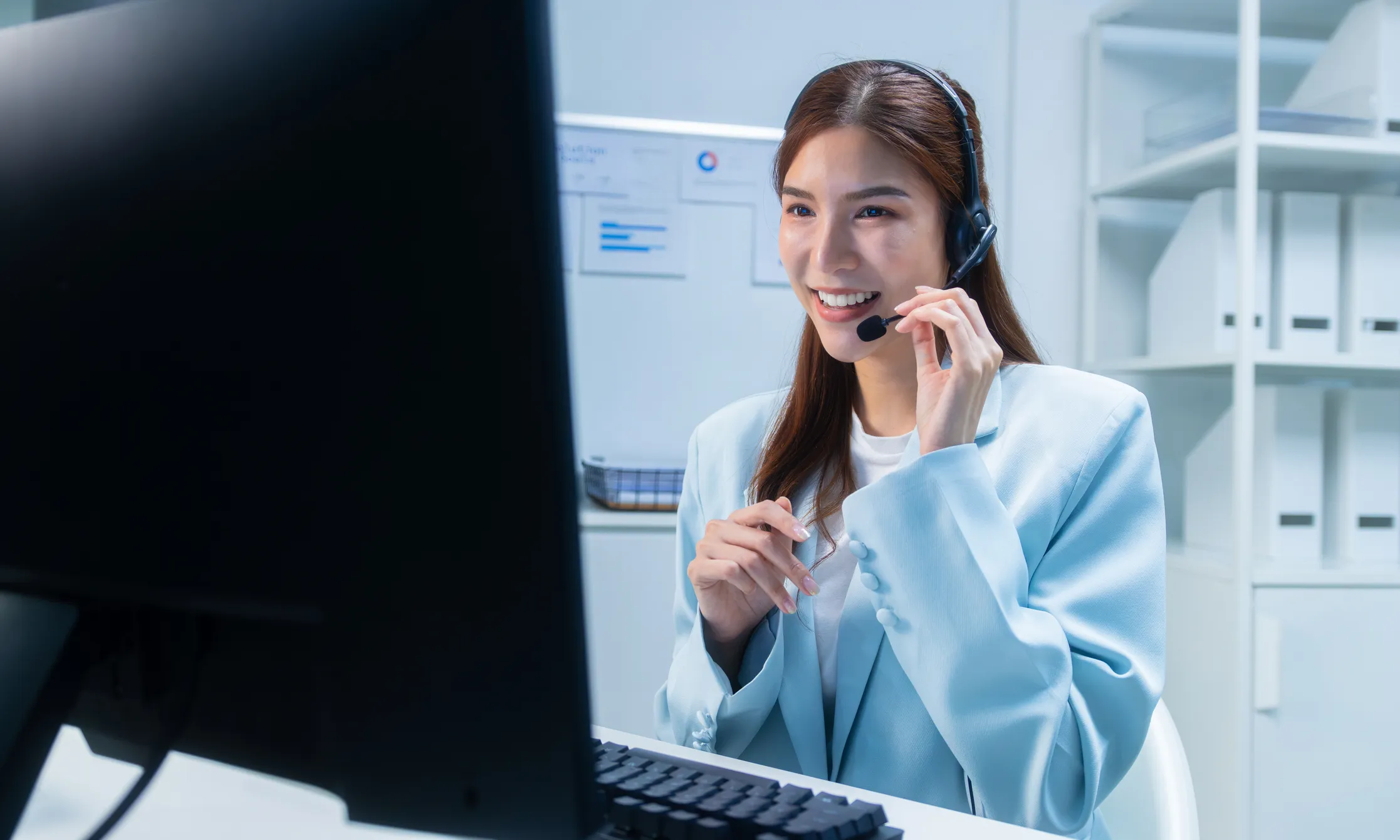 High performing teams A smiling customer service professional wearing a headset speaks with a customer while working at her computer — representing the front-line team members that high-performance leaders develop and support